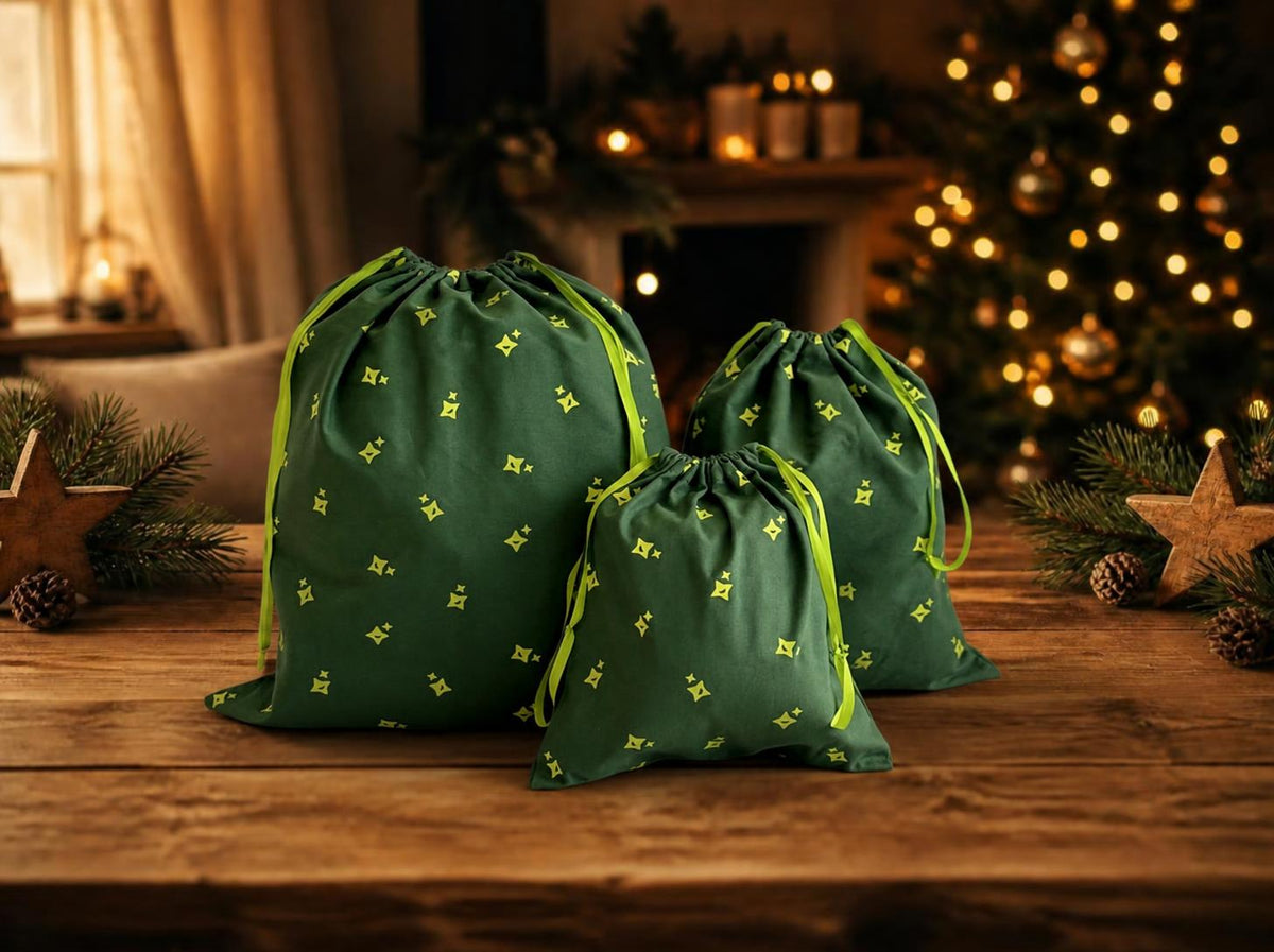 Drie katoenen ‘ MagicHolz ’-cadeauzakjes in de maten S, M en L op een houten tafel in kerstsfeer